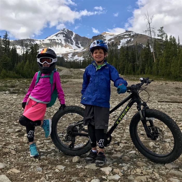 Kids standing with a mountain bike with Lone Peak in the background // Youth Bike Camps in Big Sky MT
