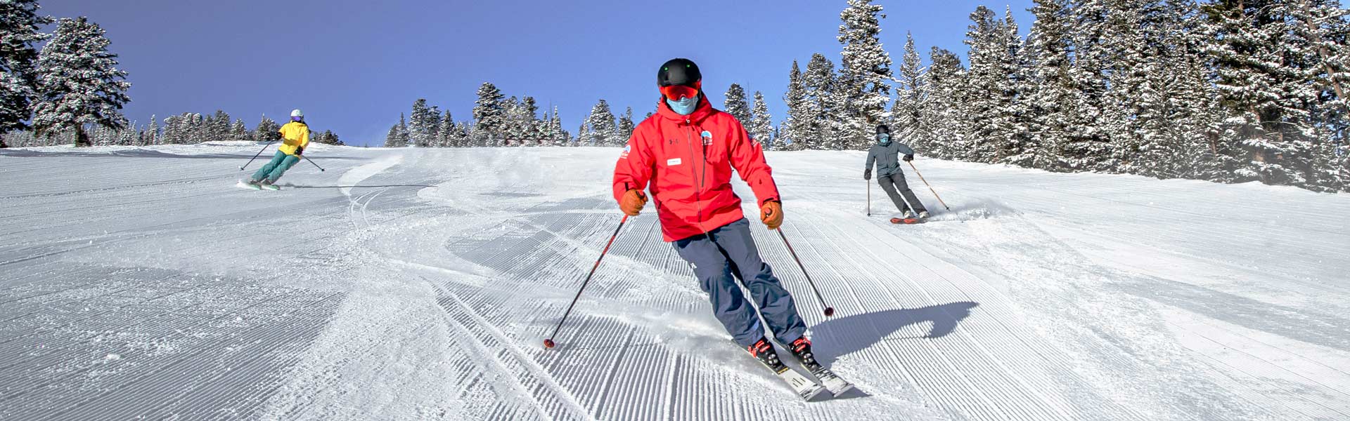 Instructor skiing a groomed runs with two skiers following them