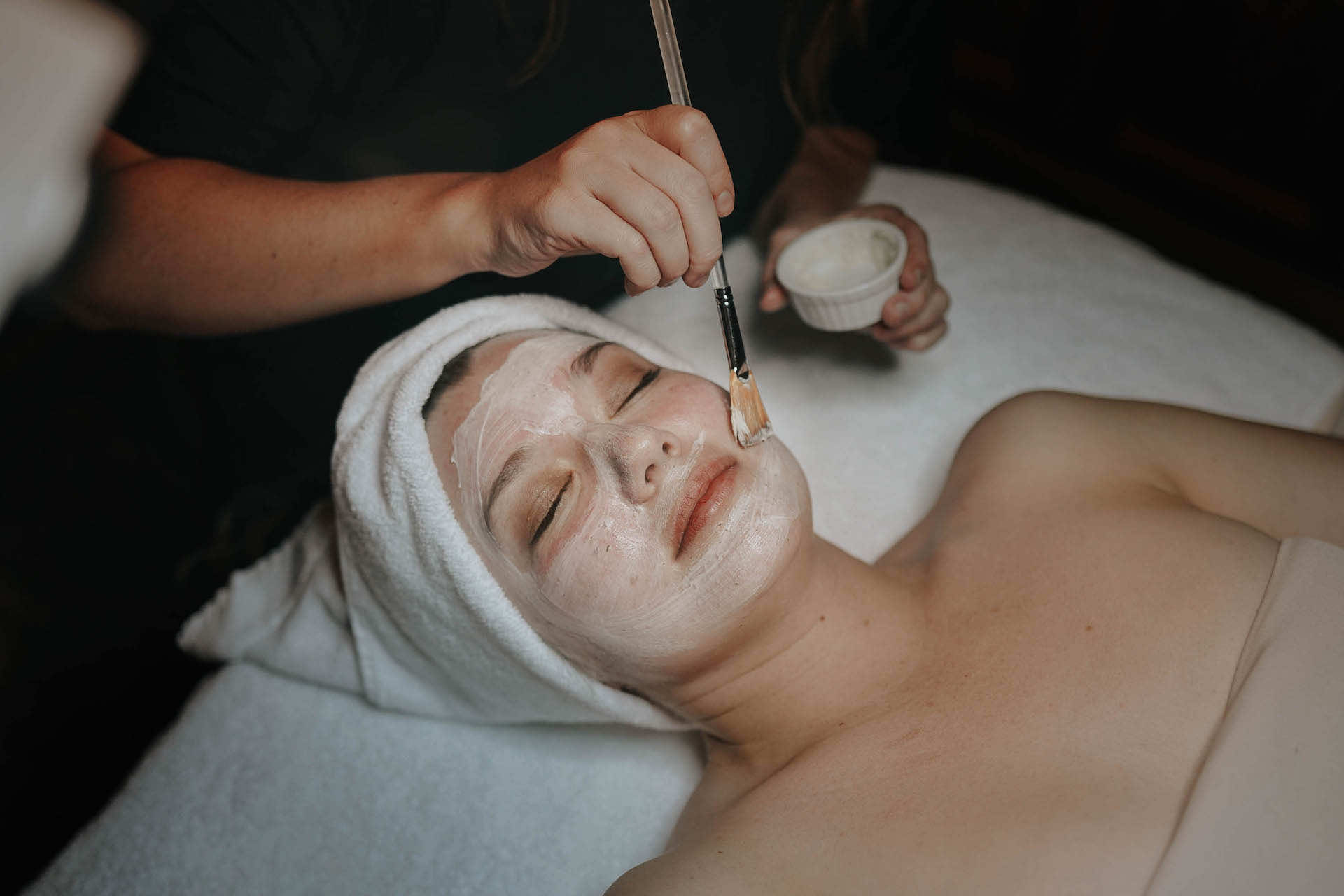 Esthetician brushing product onto a woman's face